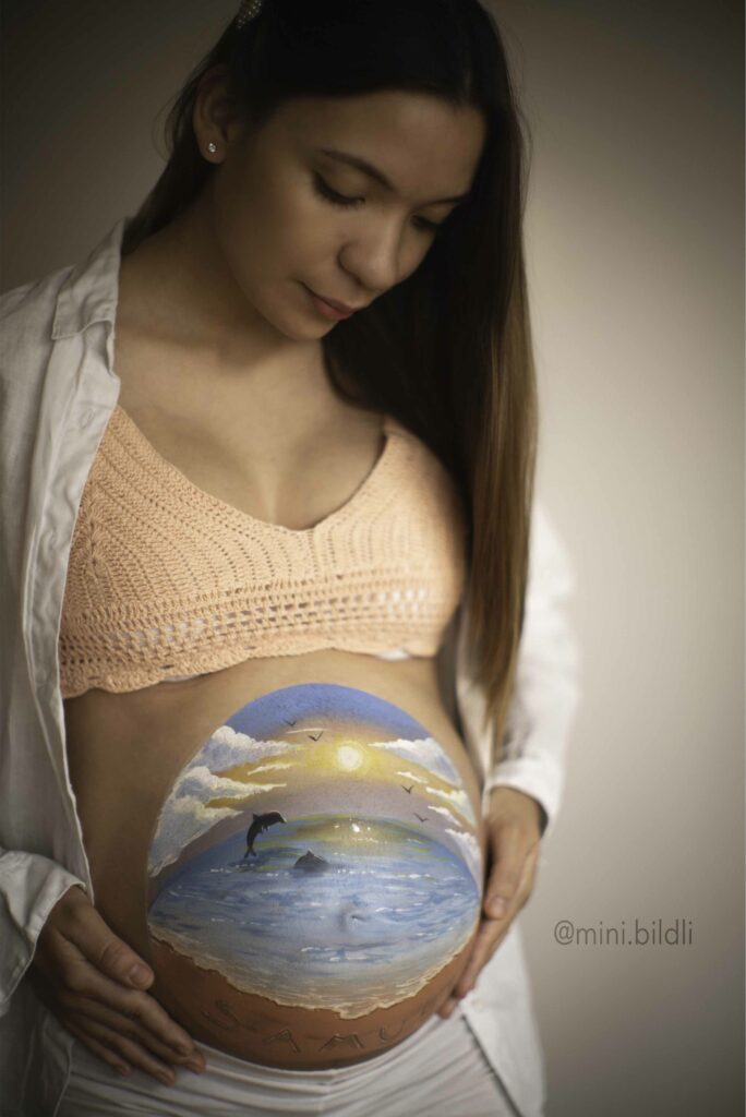Pregnant woman with Sea and beach design on her belly. He looks at her and grabs her with both hands.
